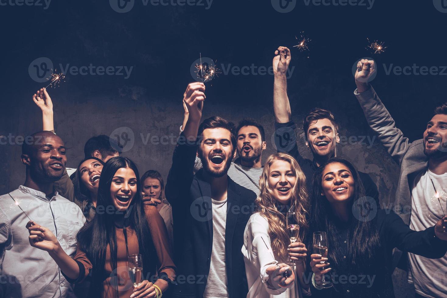 fiesta con amigos. Grupo de jóvenes alegres portando bengalas y copas de champán foto