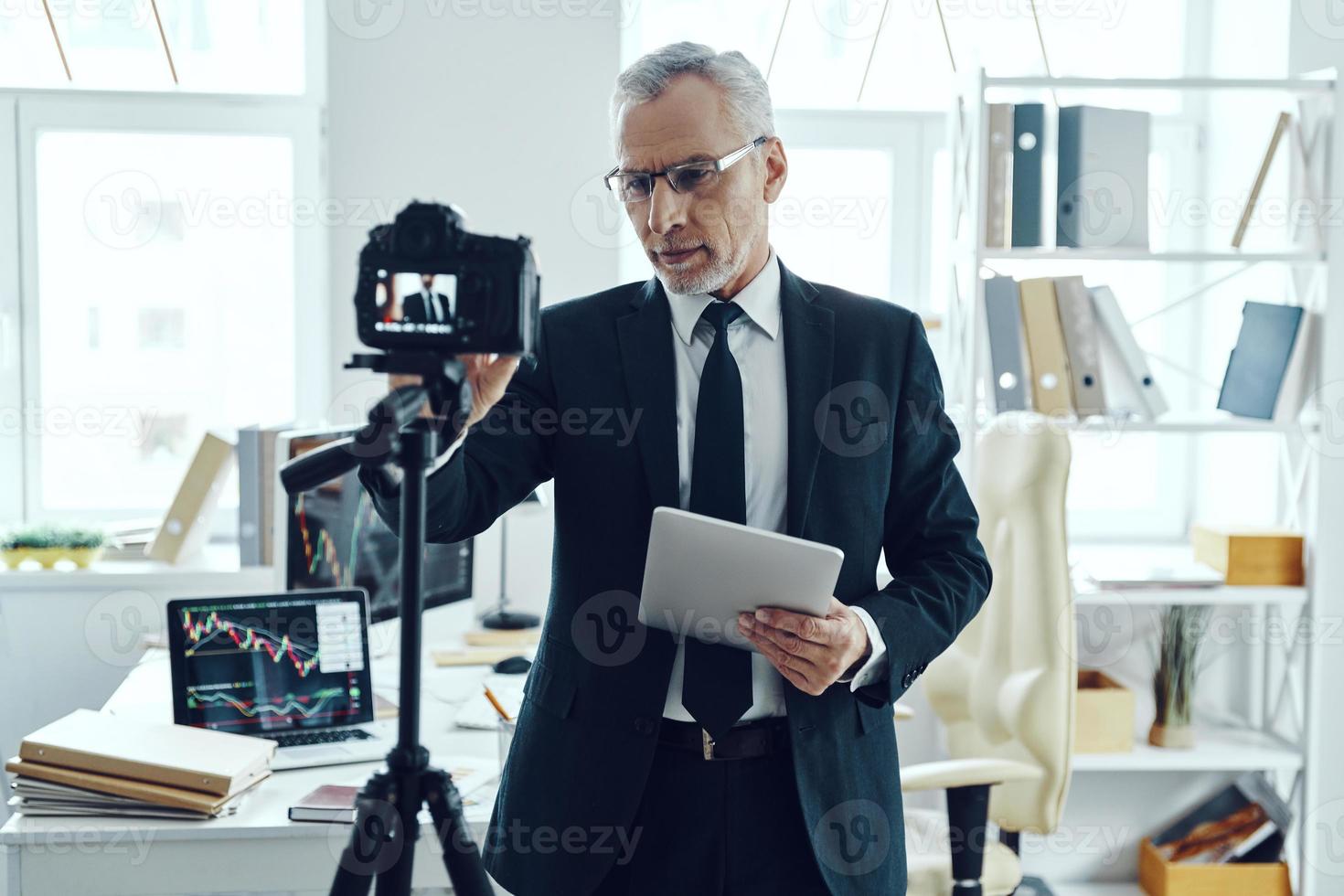 Senior man in elegant business suit adjusting video camera while making social media video photo