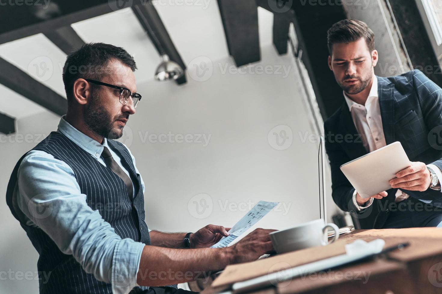 Taking care of business. Two young modern men in formalwear working together while sitting indoors photo
