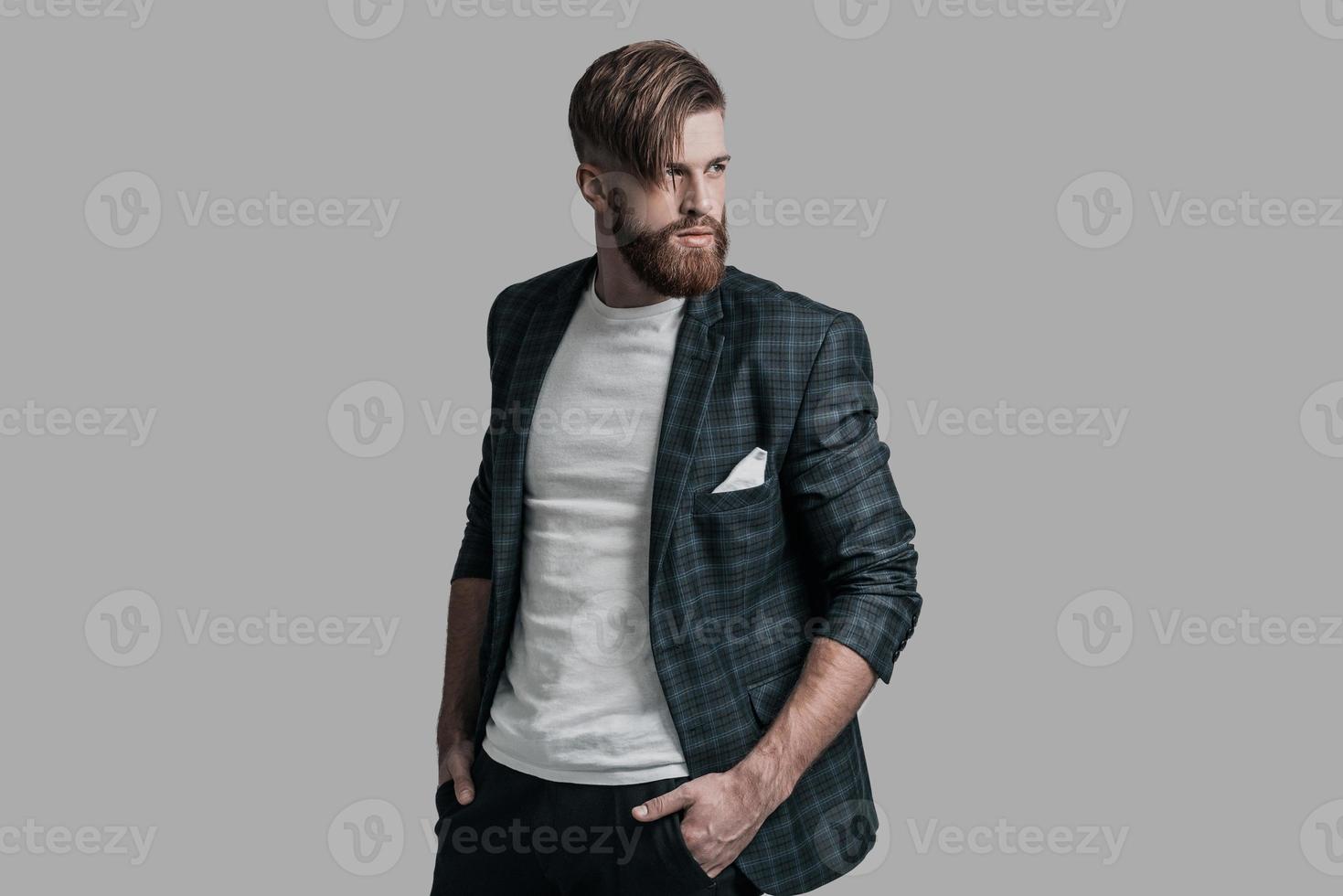 Confident and handsome. Handsome man with long hair and beard looking away while standing against grey background photo