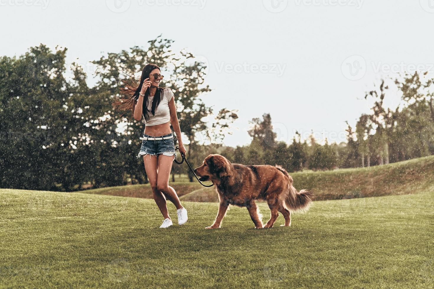 Real joy of being around. Full length of beautiful young woman playing with her dog and smiling while running outdoors photo