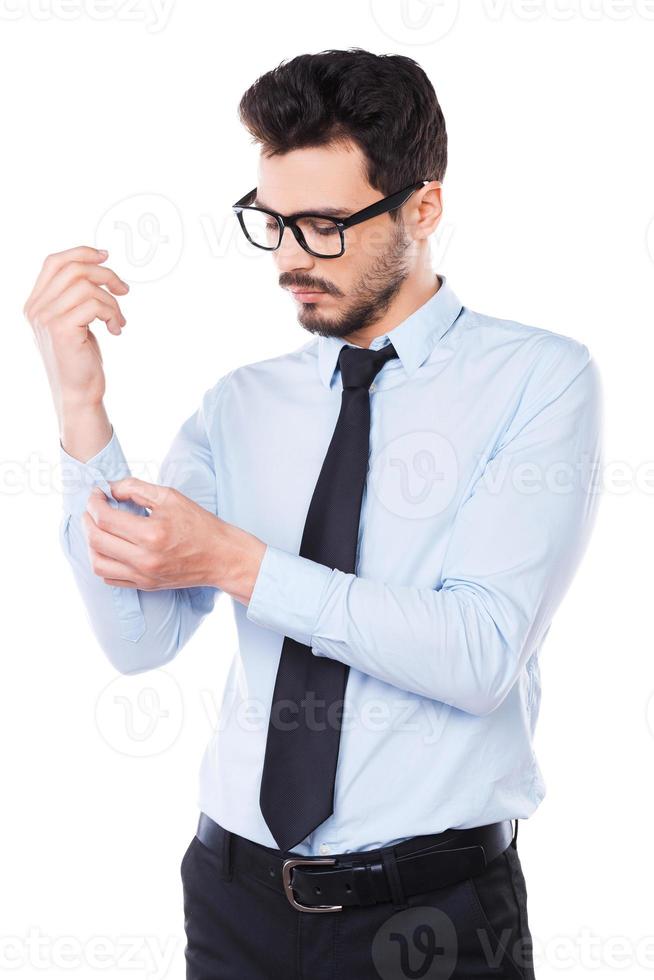 Everything should be perfect. Confident young man in shirt and tie adjusting his sleeve while standing against white background photo