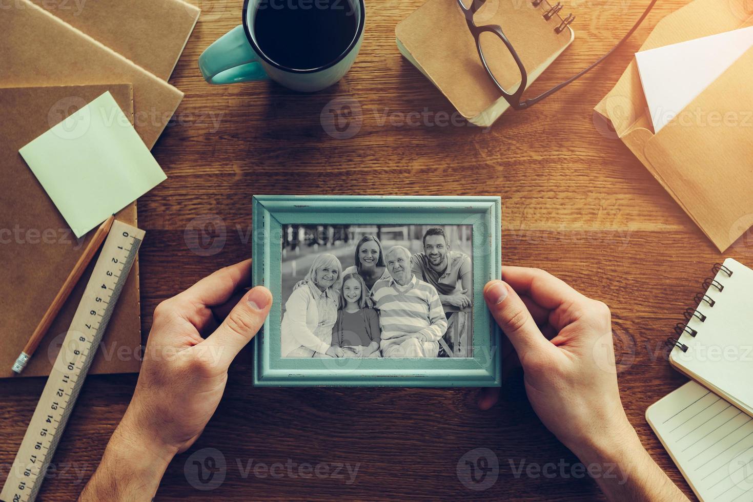 My family is my inspiration. Close-up top view of man holding photograph of his family over wooden desk with different chancellery stuff laying around photo