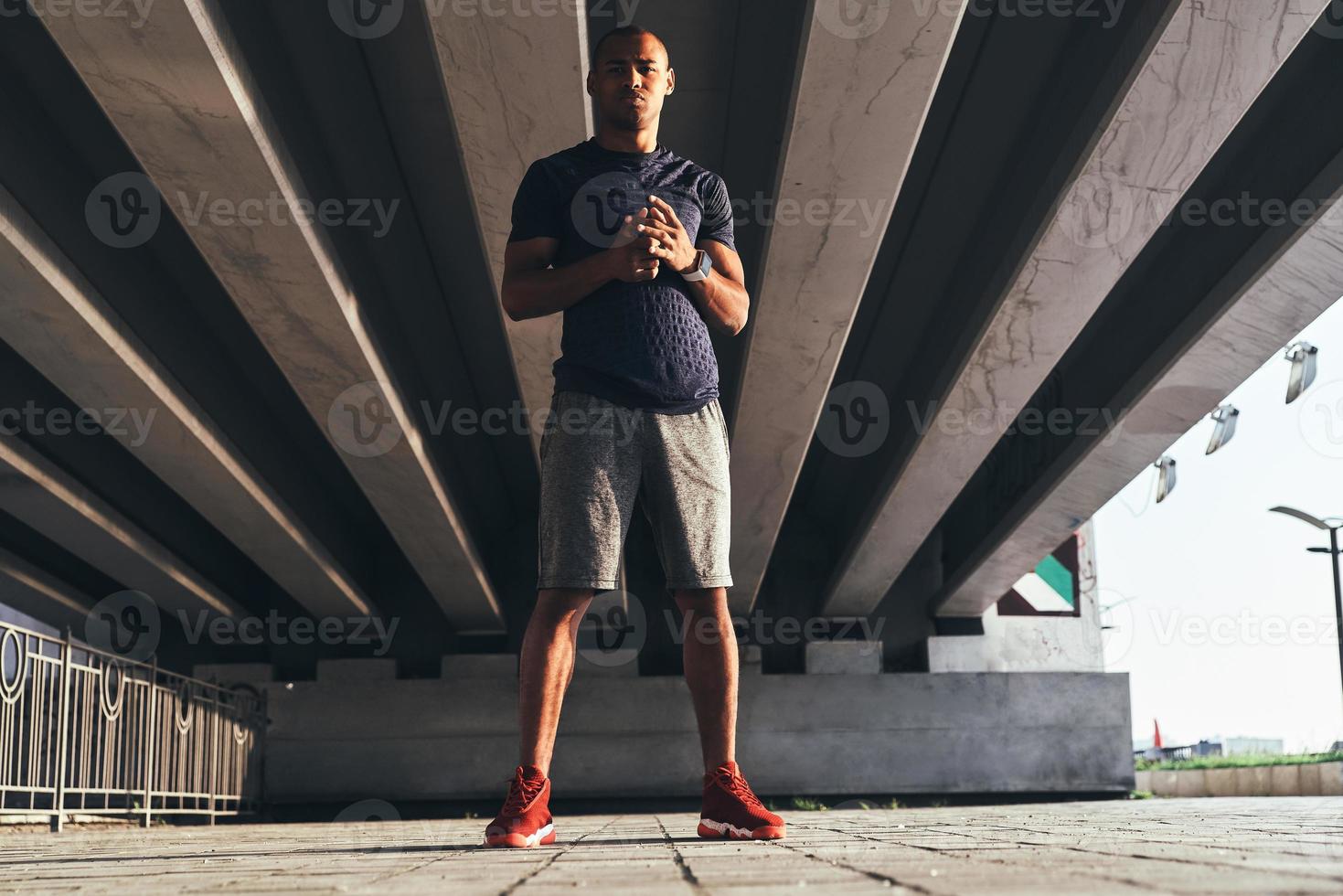 Serious about staying in shape. Full length of young African man in sports clothing looking at camera and keeping hands clasped while standing outdoors photo