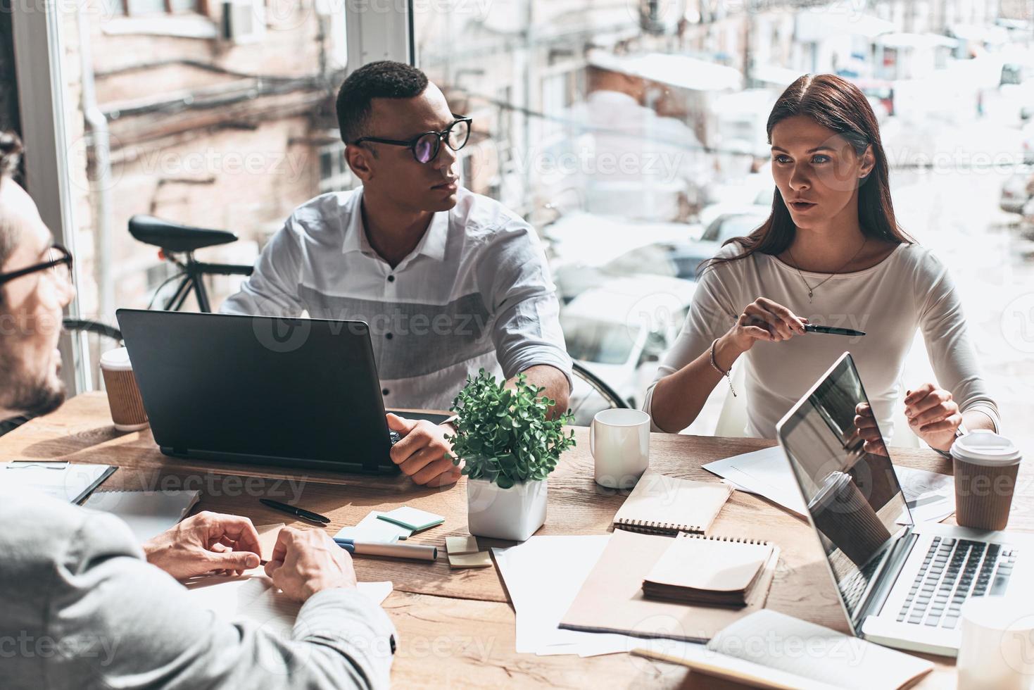 ajetreado día de trabajo. vista superior de los jóvenes modernos con ropa informal inteligente discutiendo negocios mientras están sentados en la oficina creativa foto