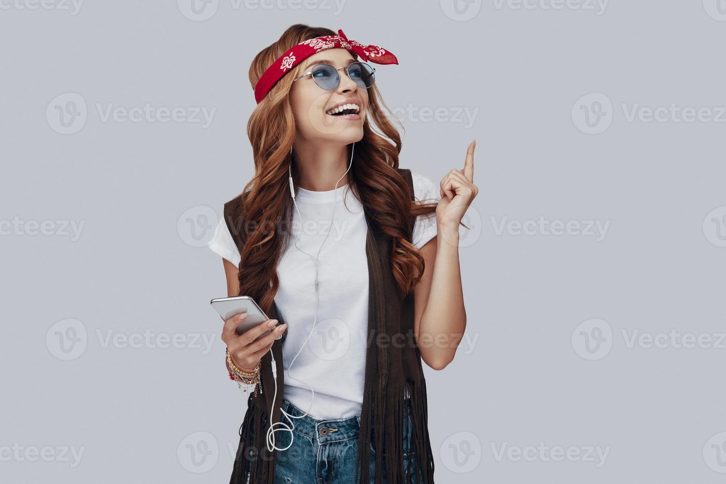 Attractive stylish young woman listening music and smiling while standing against grey background photo
