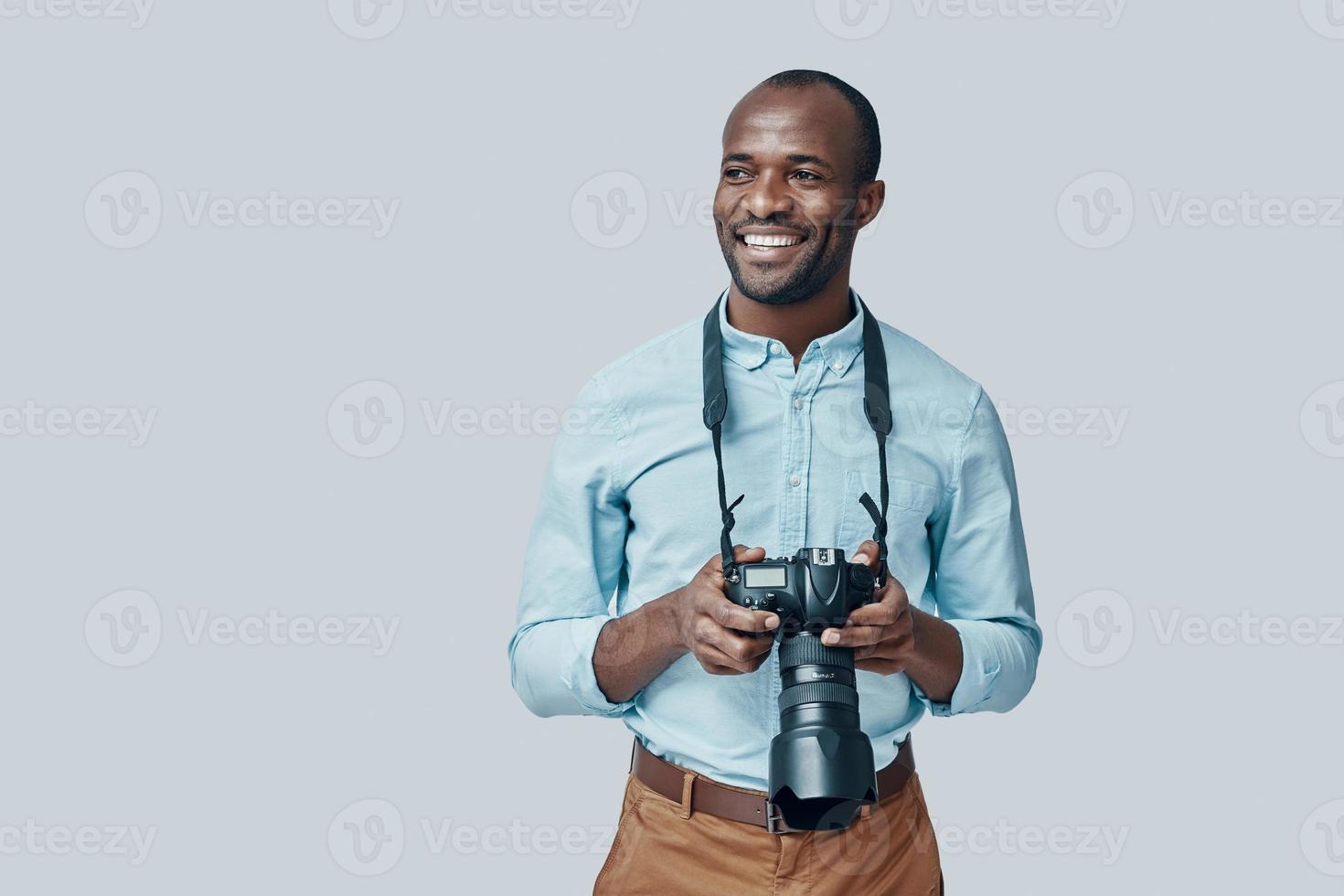 Handsome young African man looking away and smiling while standing against grey background photo