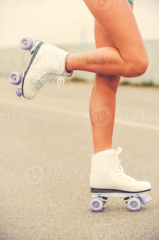 Ready to roller skating. Close-up of young woman in roller skates lifting her leg up while standing outdoors photo