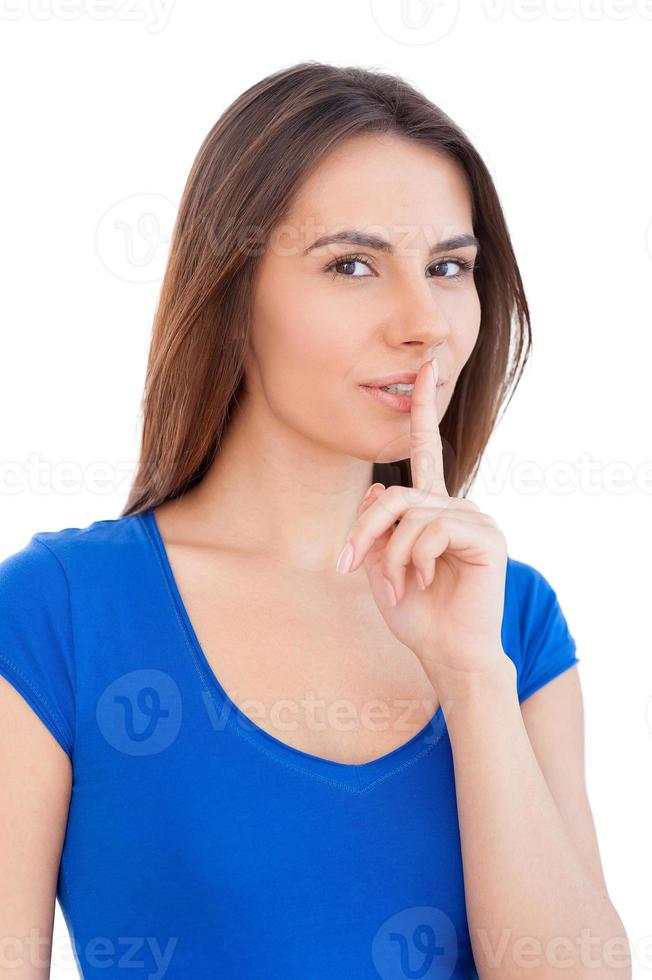 Keep silence Beautiful young woman looking at camera and holding finger on lips while standing isolated on white photo