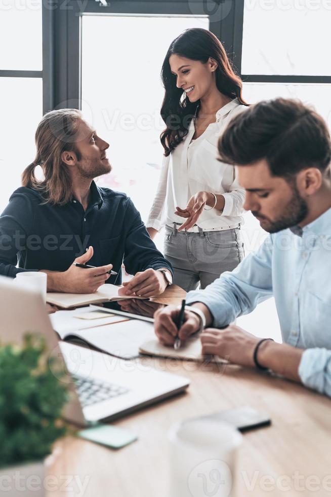 Achieving best results together. Young modern colleagues in smart casual wear working together and smiling while spending time in the office photo