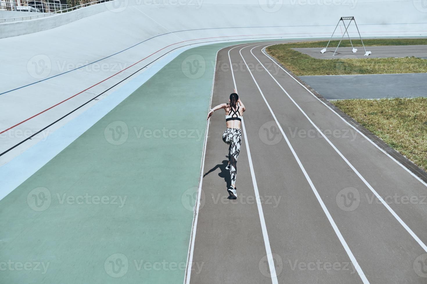 Making effort. Top rear view of young woman in sports clothing running while exercising outdoors photo