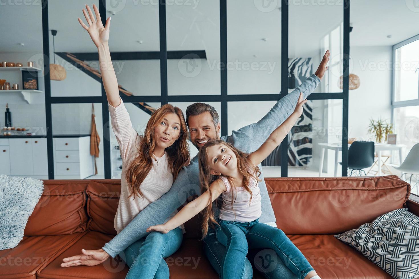 familia joven feliz sonriendo y mirando a la cámara mientras se unen en casa foto