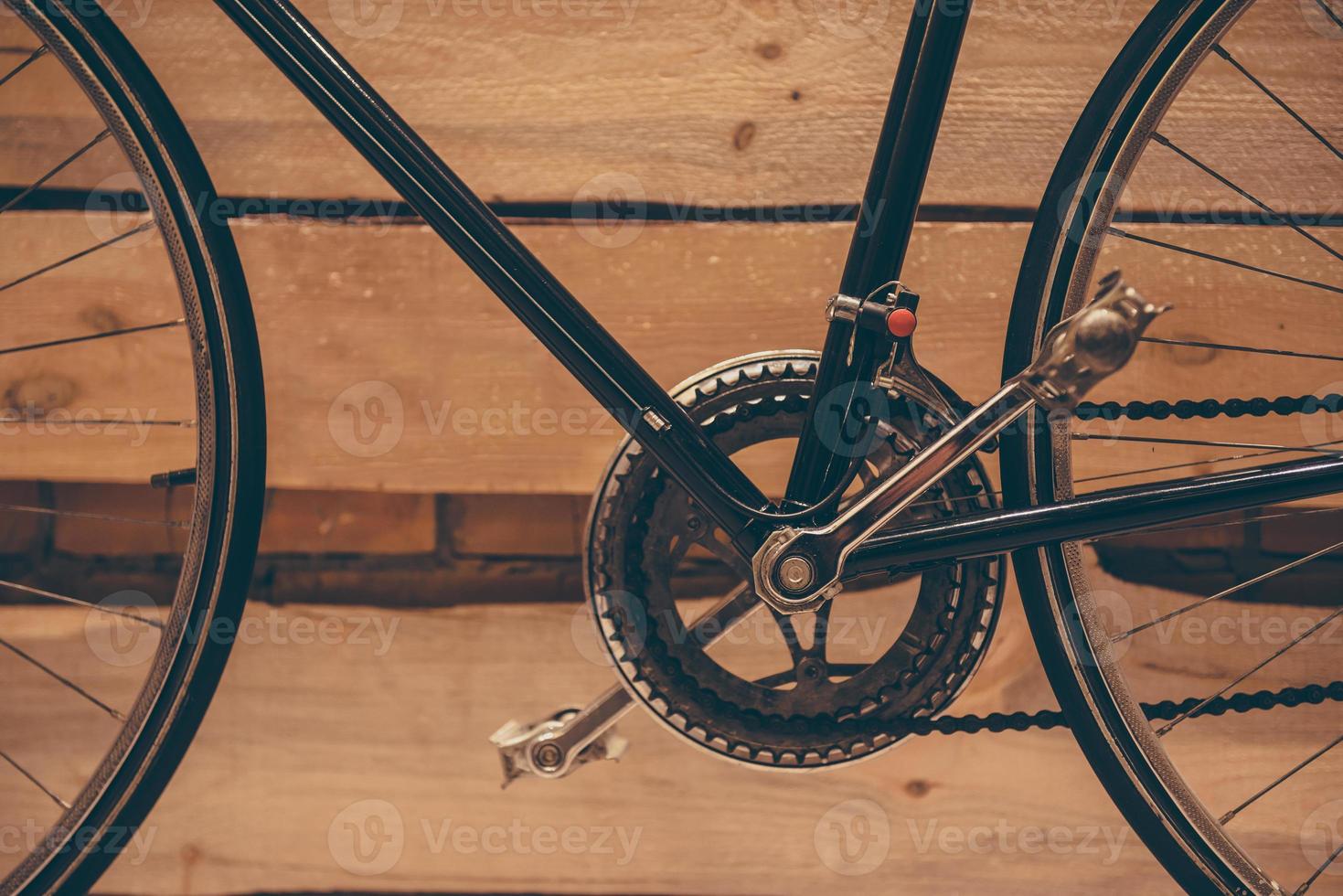 Part of bicycle. Close-up of retro styled bicycle standing against rough wooden wall photo