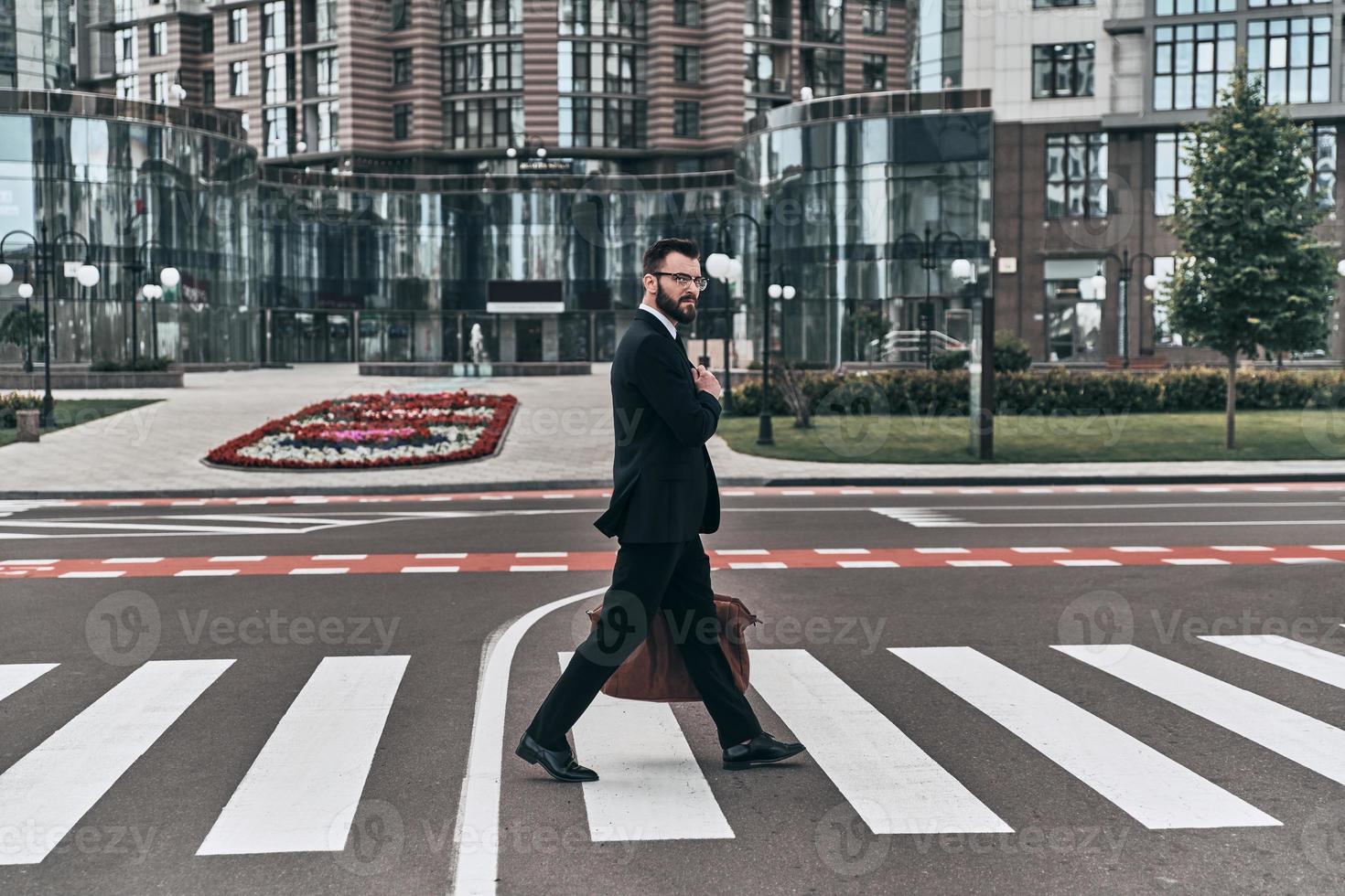 siempre cuidadoso toda la longitud de un joven con traje completo cruzando la calle mientras camina al aire libre foto