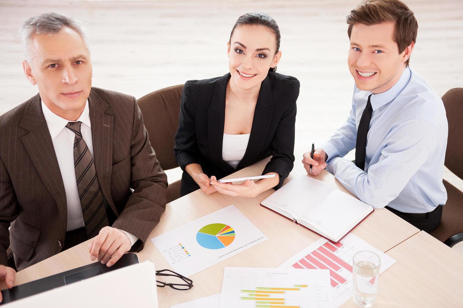 Business people at work. Top view of three confident business people in formalwear working together while sitting together at the table and smiling photo