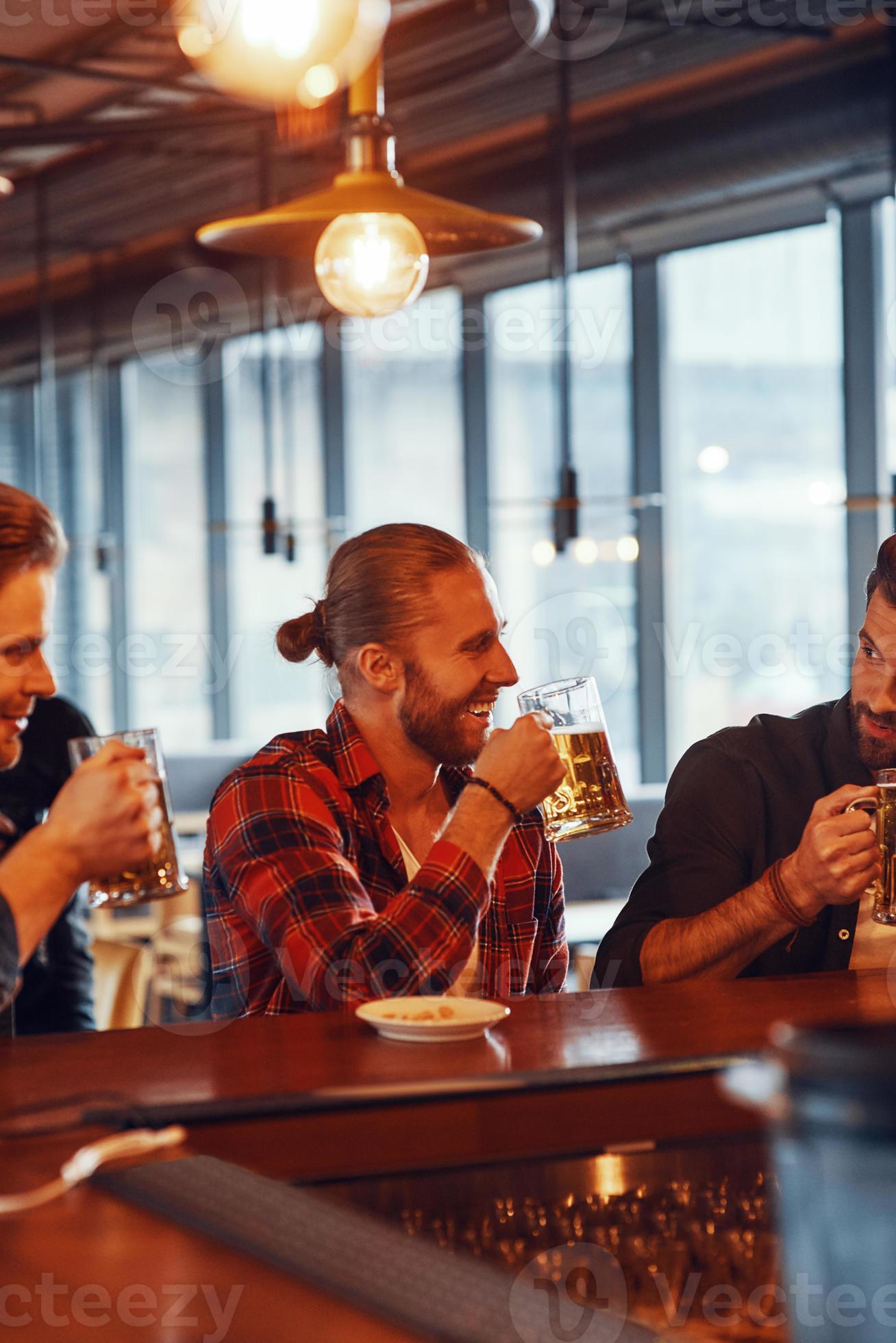Happy young men in casual clothing enjoying beer and smiling while