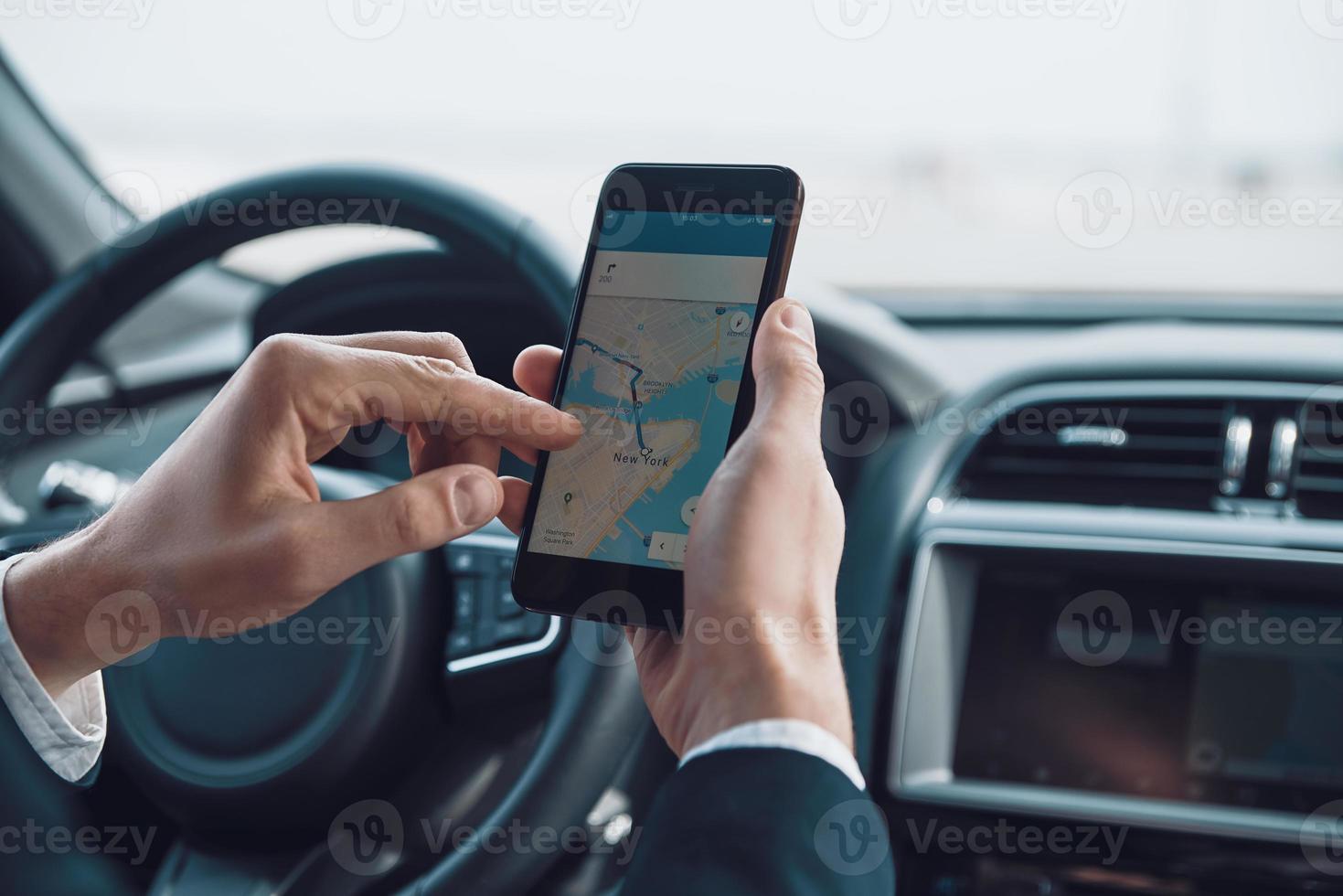 Checking the direction. Close up of young man using smart phone to check the map while driving a car photo