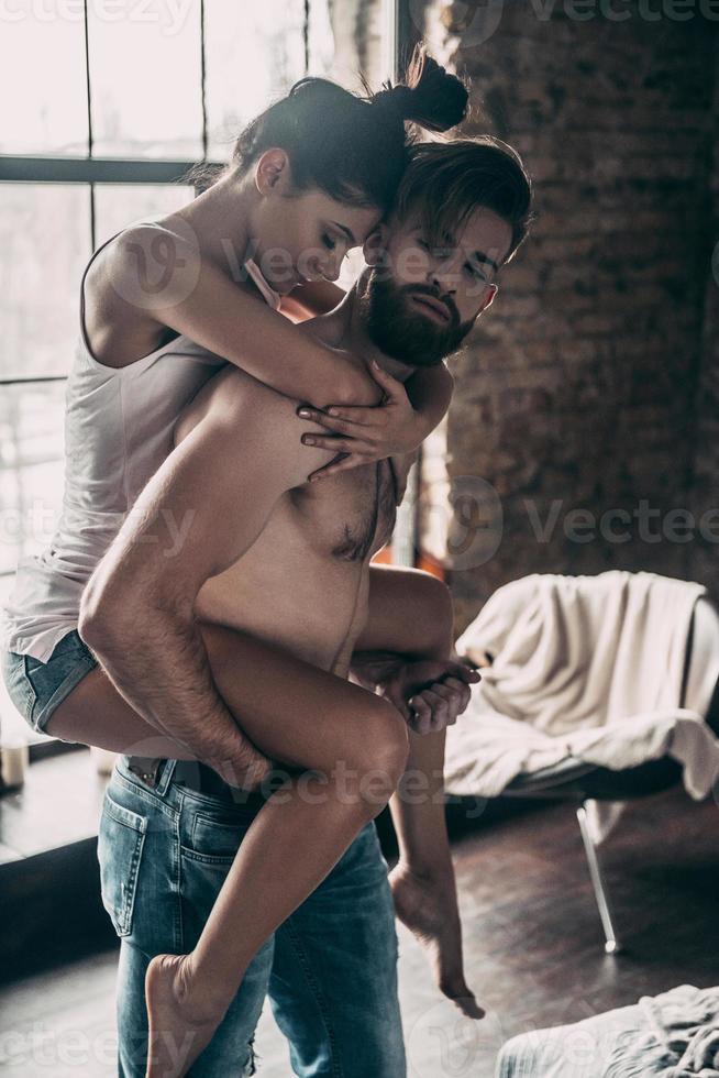 Real love. Young beautiful couple enjoying free time at home while shirtless man carrying attractive woman on shoulders photo