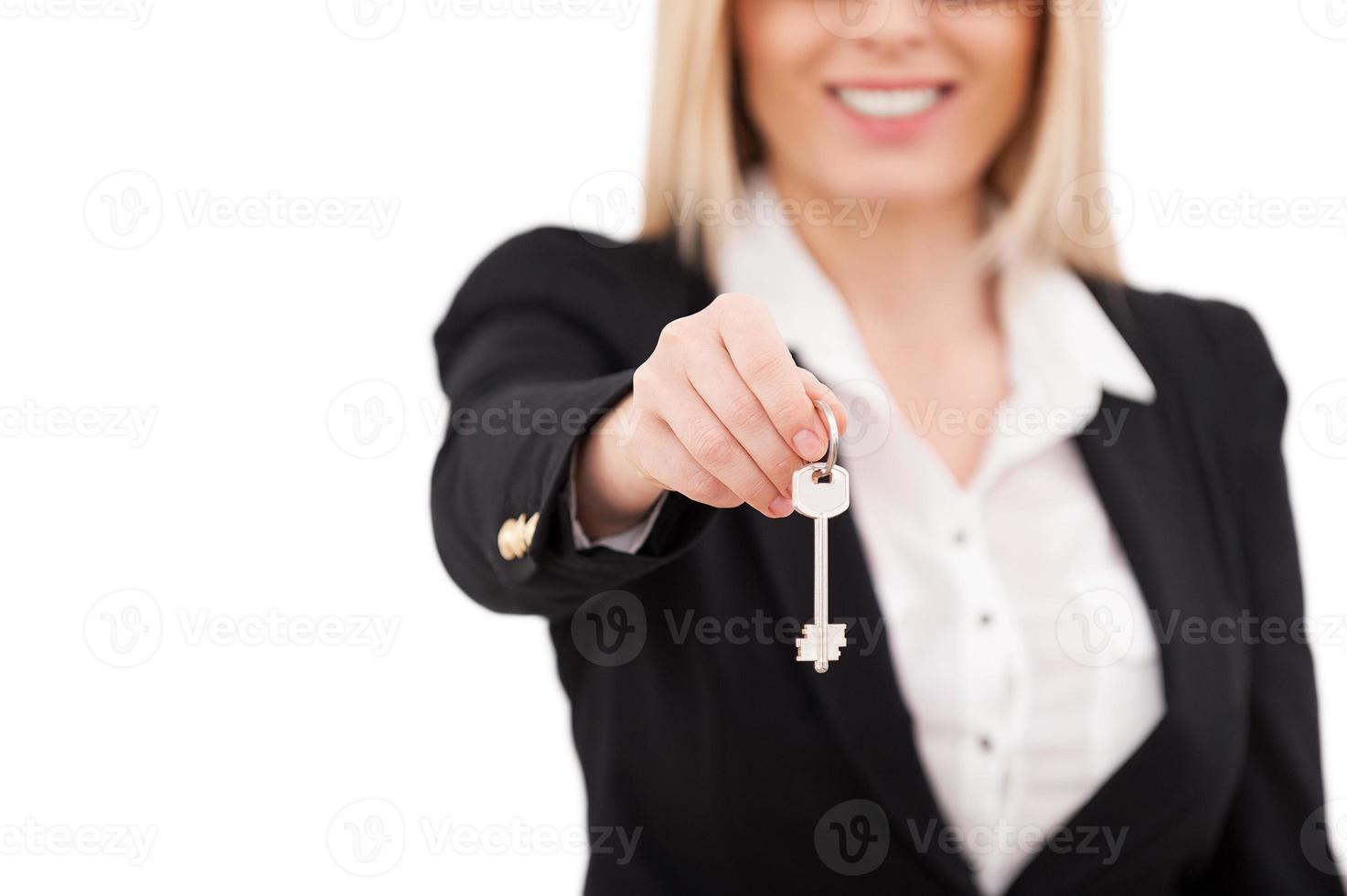 Here is your key Cropped image of mature businesswoman stretching out key and smiling while standing isolated on white photo