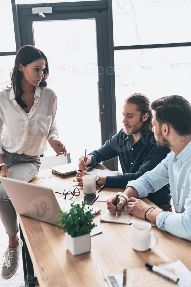 Concentrated at work. Young modern colleagues in smart casual wear working together and smiling while spending time in the office photo