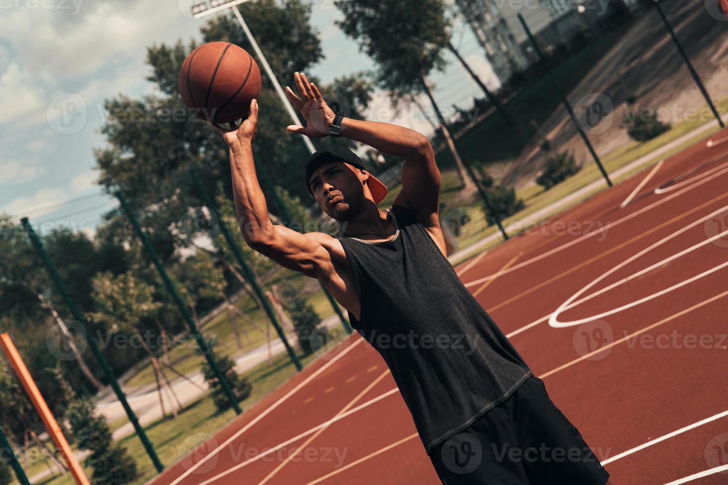 Full of energy. Young African man in sports clothing throwing a ball while playing basketball outdoors photo