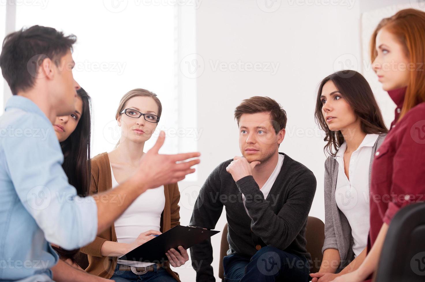I want to share my problem. Group of people sitting close to each other while man telling something and gesturing photo