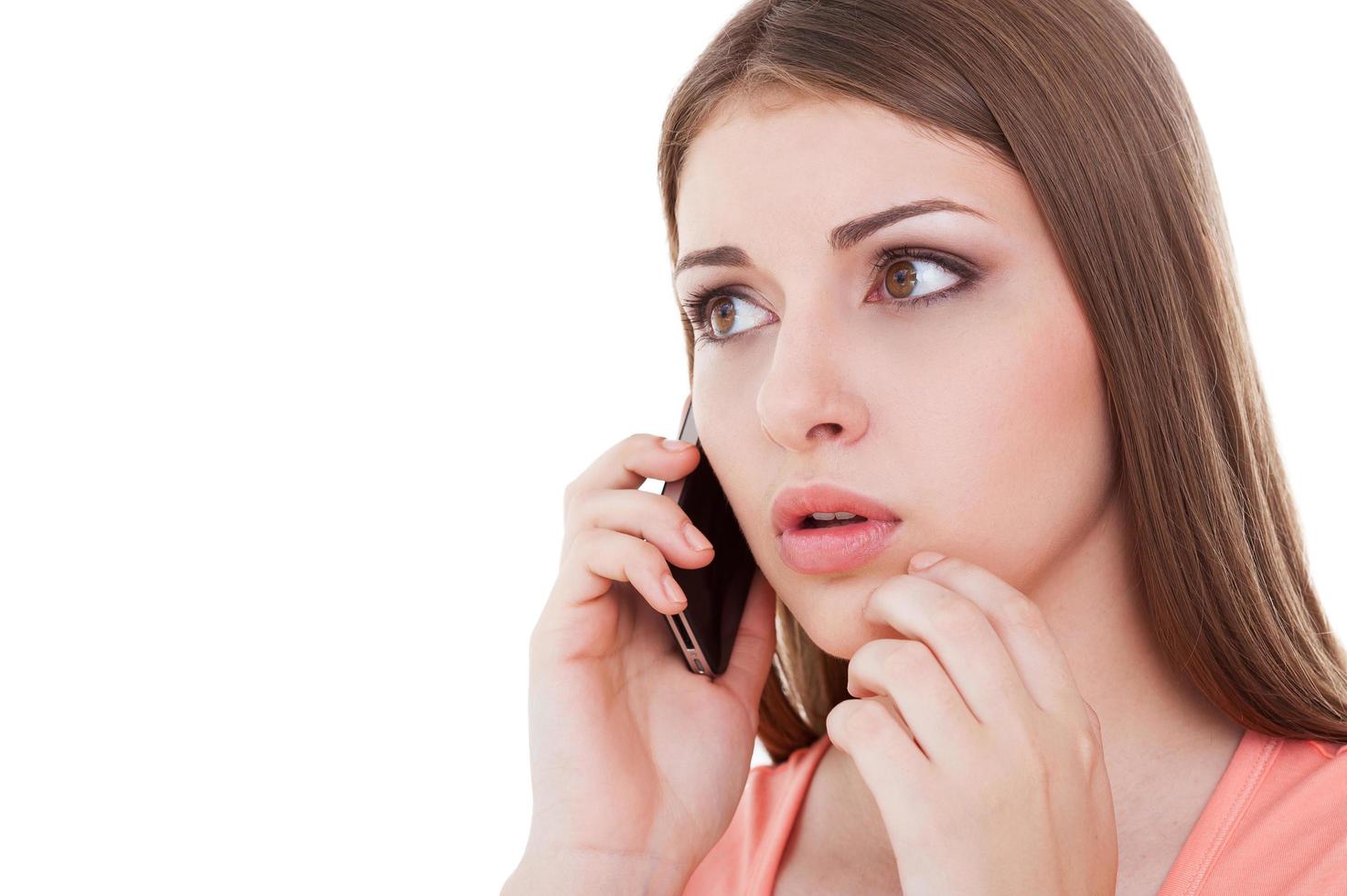 Bad news. Frustrated young woman talking on the mobile phone and looking worried while standing isolated on white photo