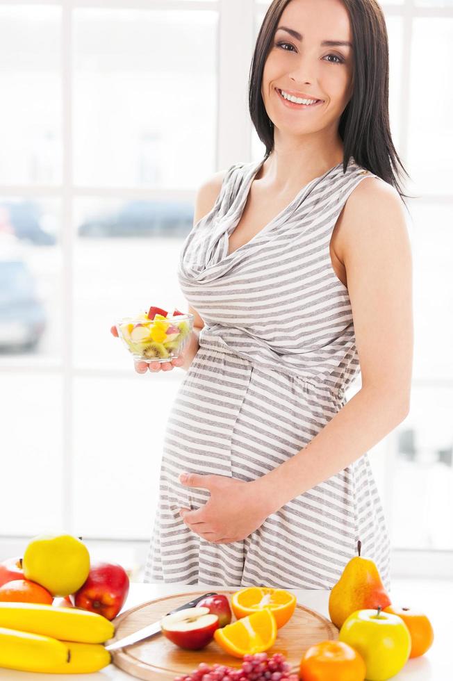 solo comida fresca y sana para mi bebe. imagen recortada de una mujer embarazada sosteniendo un plato con ensalada de frutas foto