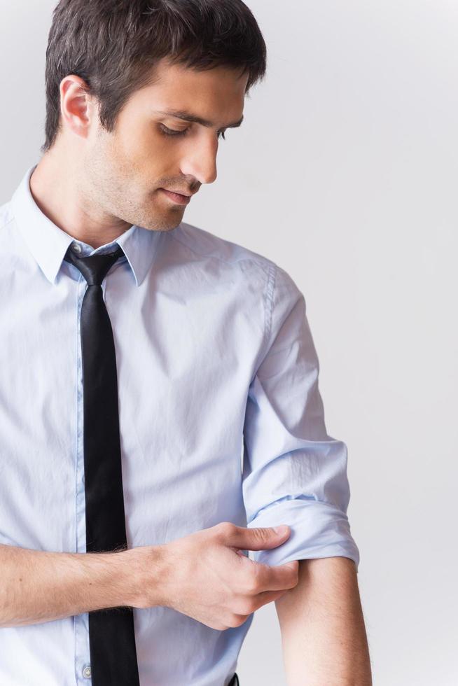 Ready to work. Confident young man in shirt and tie adjusting his sleeve while standing against grey background photo