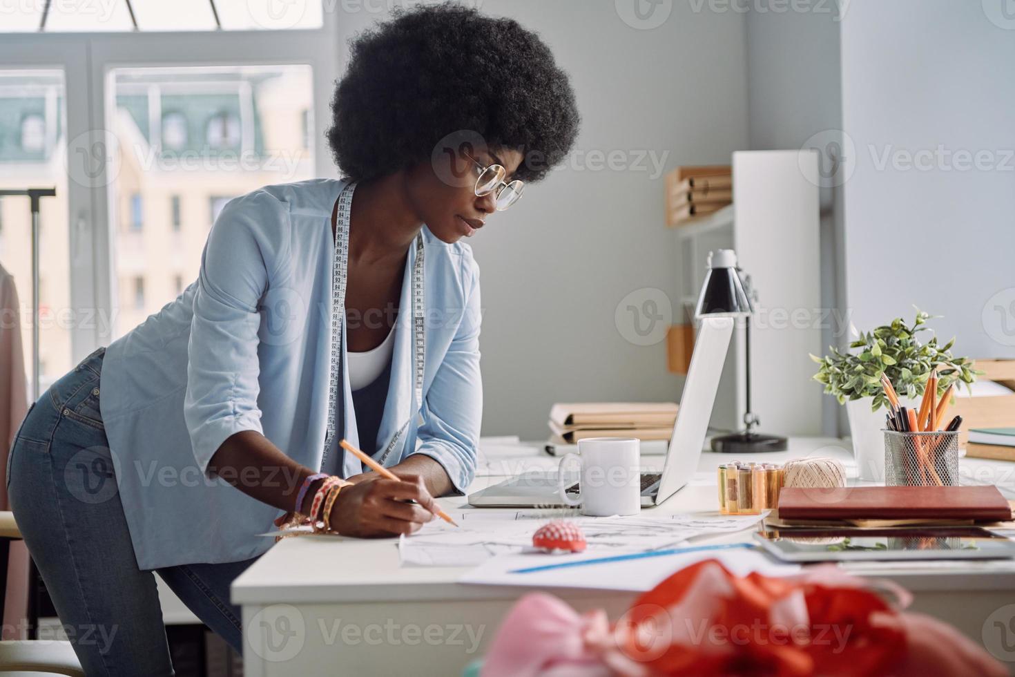 Beautiful young African woman working in fashion design studio photo