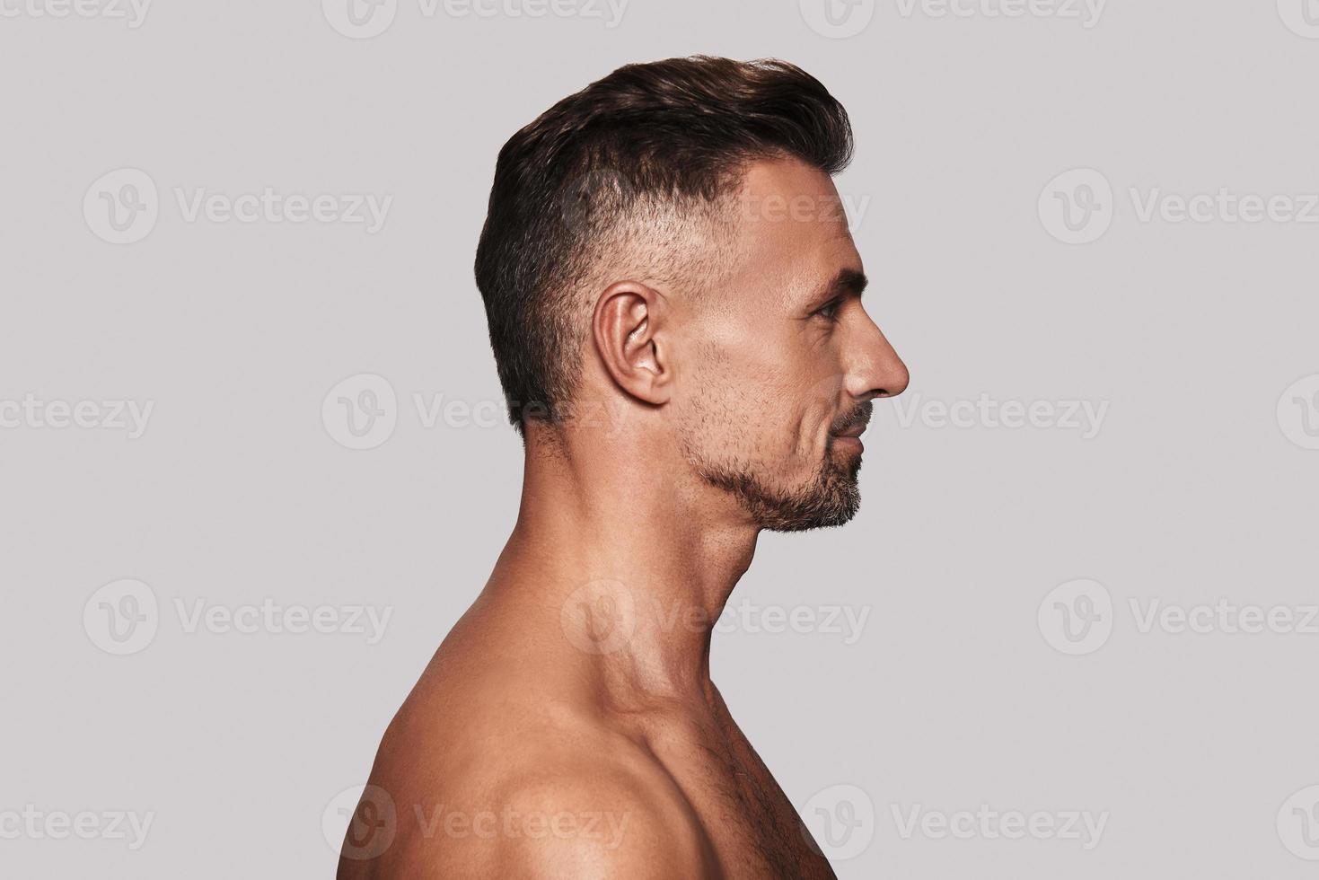 Shirtless man. Side view of good looking young man smiling while standing against grey background photo