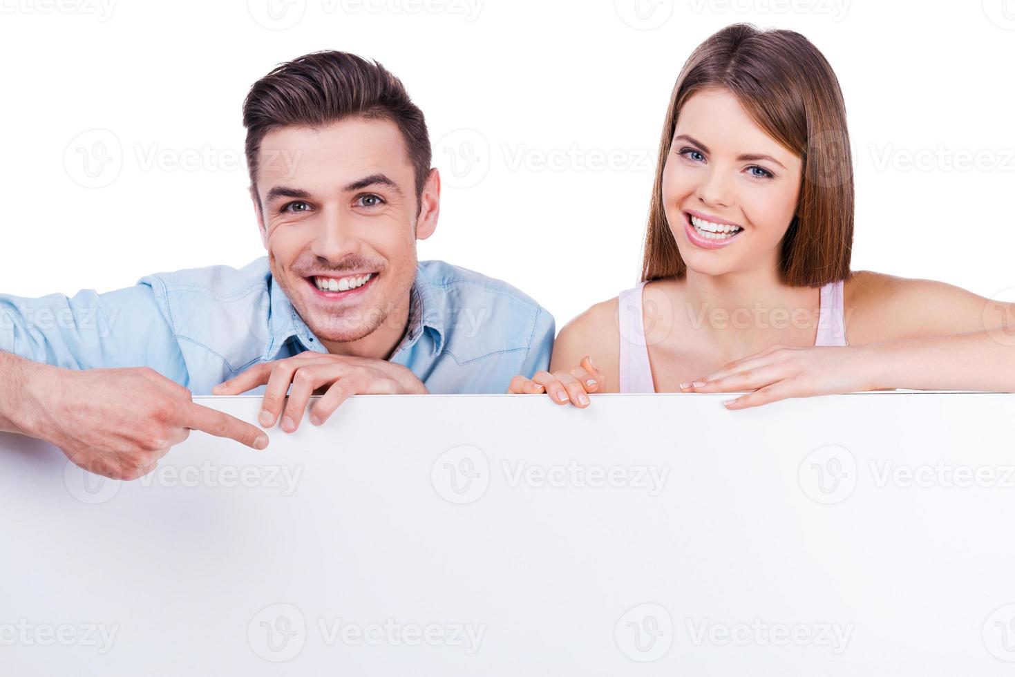 Just look at that Beautiful young loving couple smiling and leaning at copy space while man pointing it with finger photo