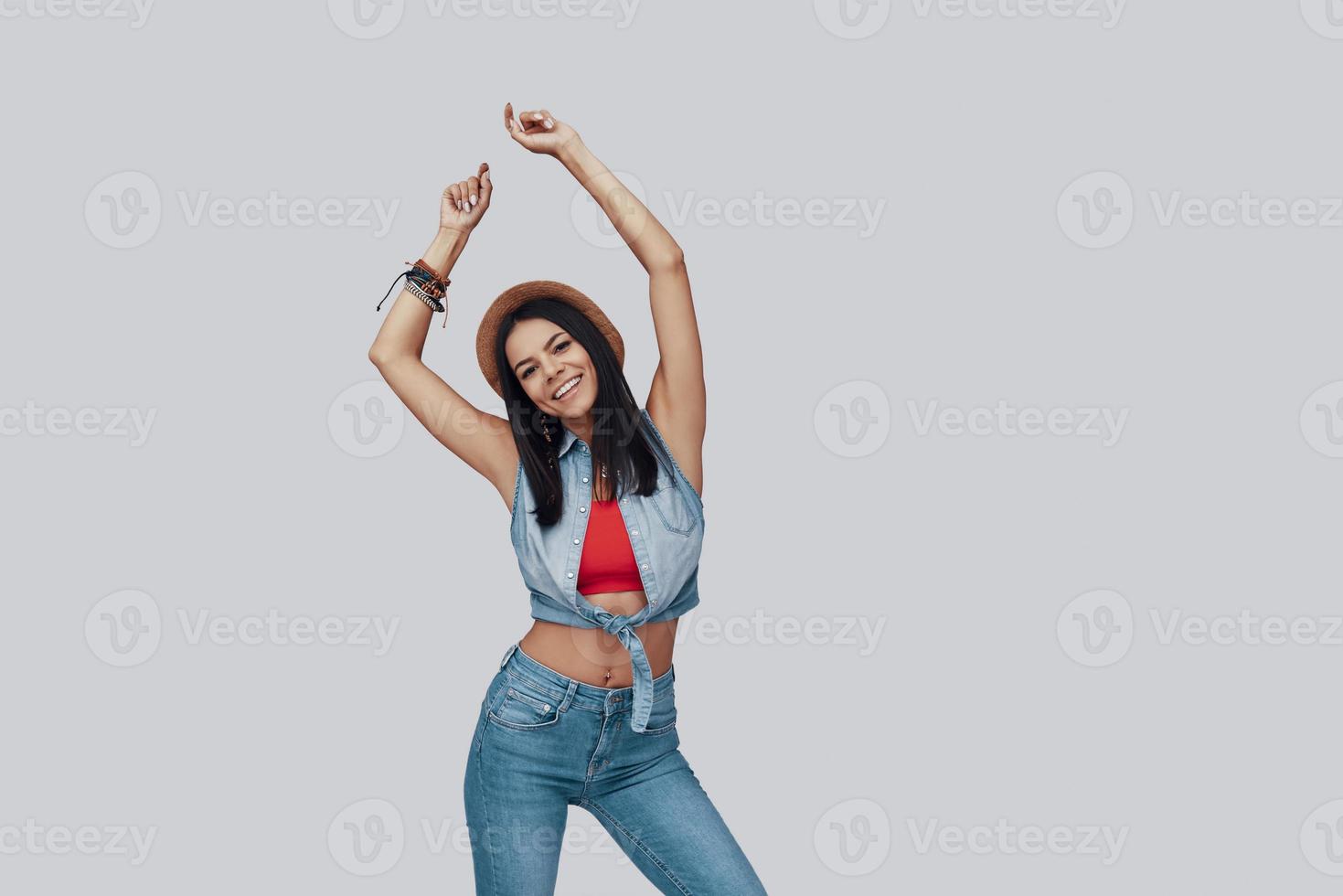 Attractive stylish young woman looking at camera and smiling while standing against grey background photo