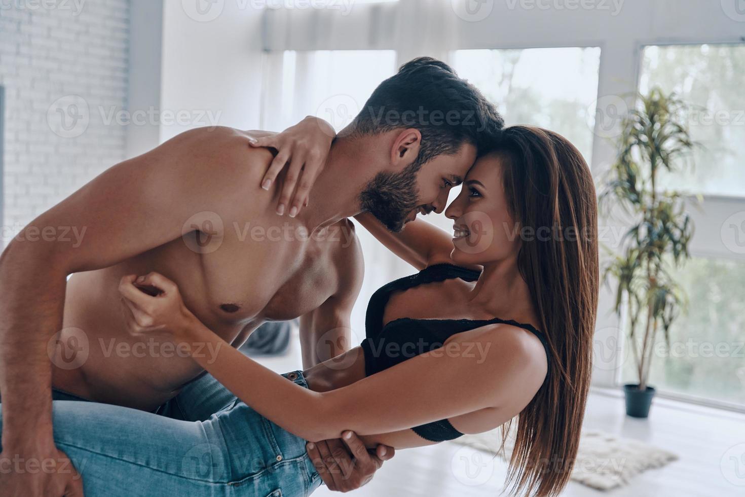 Falling in love. Beautiful young couple embracing and smiling while standing face to face in the bedroom photo