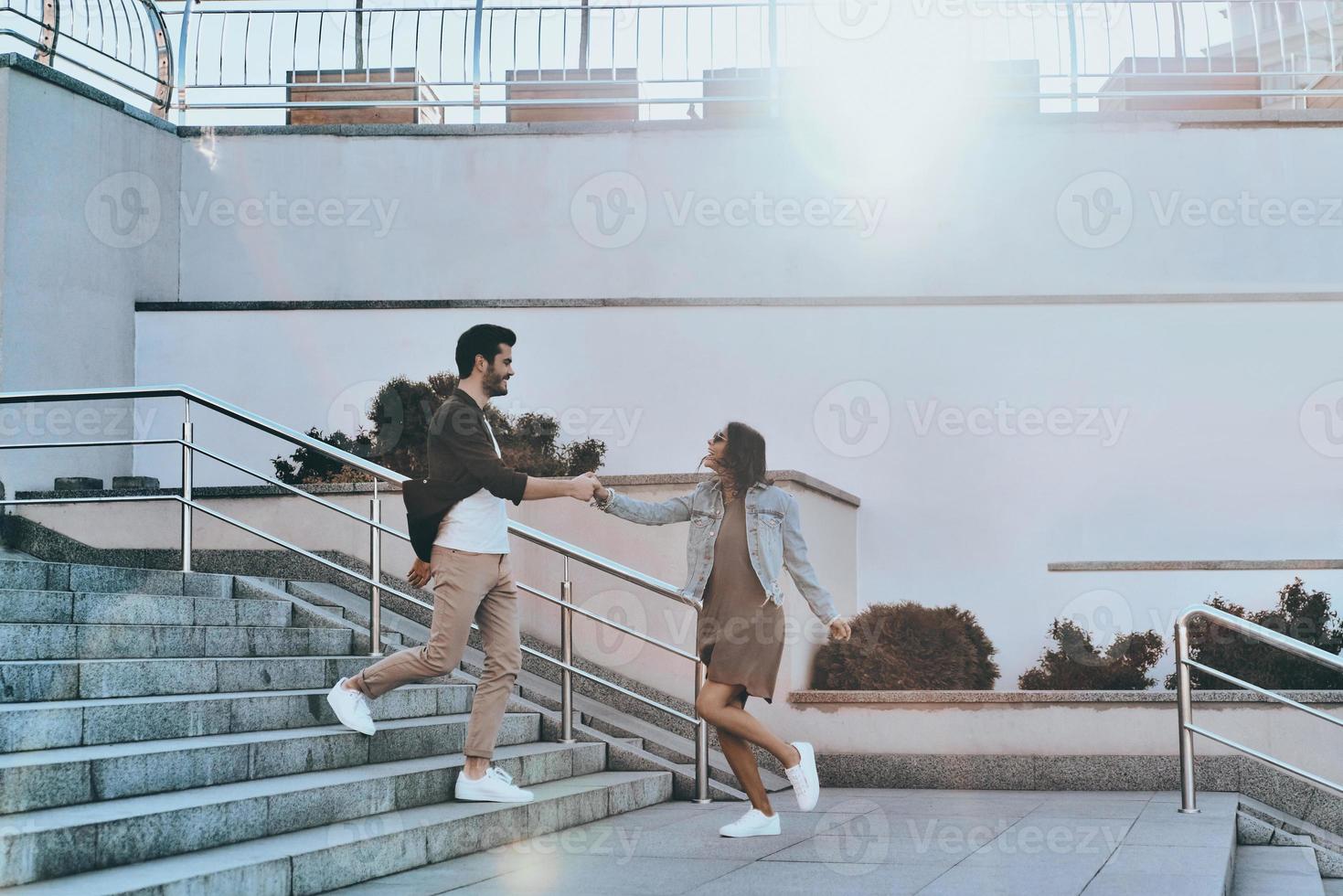 Going crazy together. Full length of handsome man and young attractive woman holding hands while walking down the stairs outdoors photo