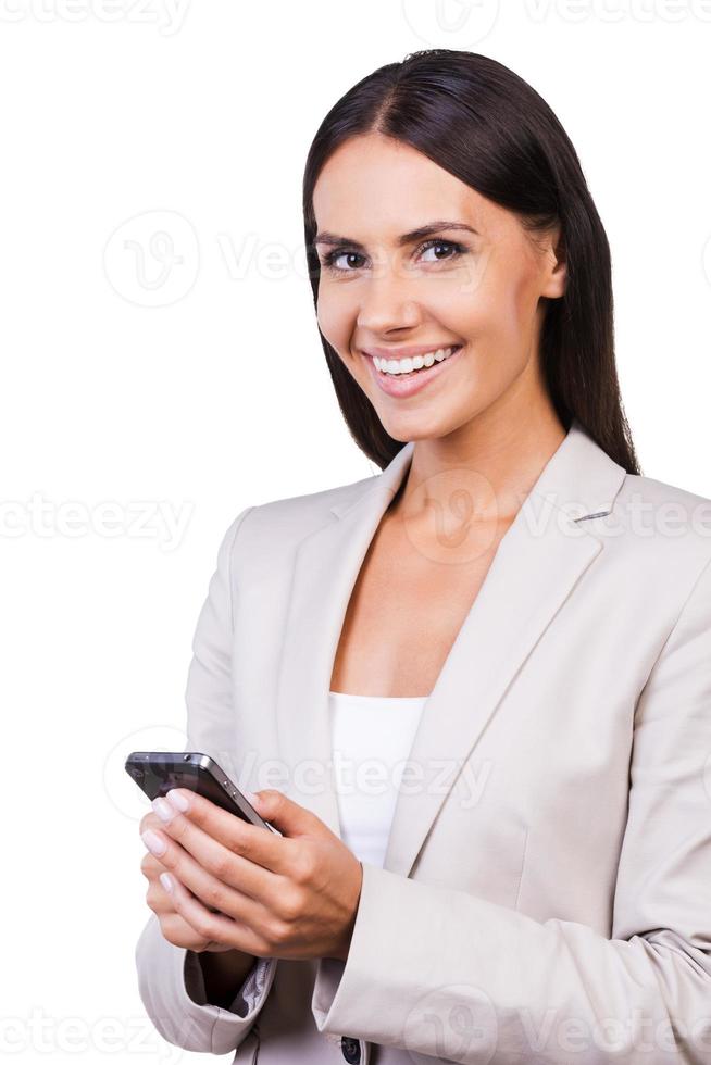 Typing business message. Confident young businesswoman in suit holding mobile phone and smiling while standing isolated on white background photo