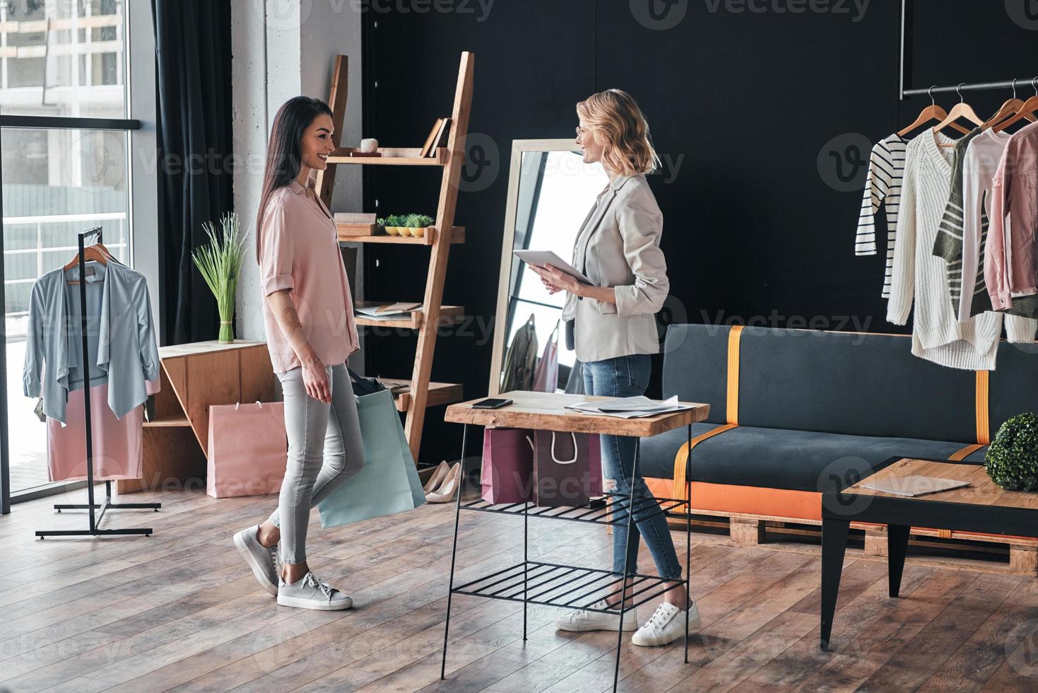 saludando a un cliente. toda la longitud de una hermosa joven entrando a la boutique mientras el estilista de moda la saluda foto