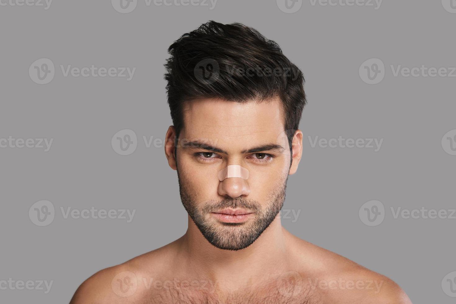 Still irresistible. Handsome young man with adhesive bandage on his nose looking at camera while standing against grey background photo