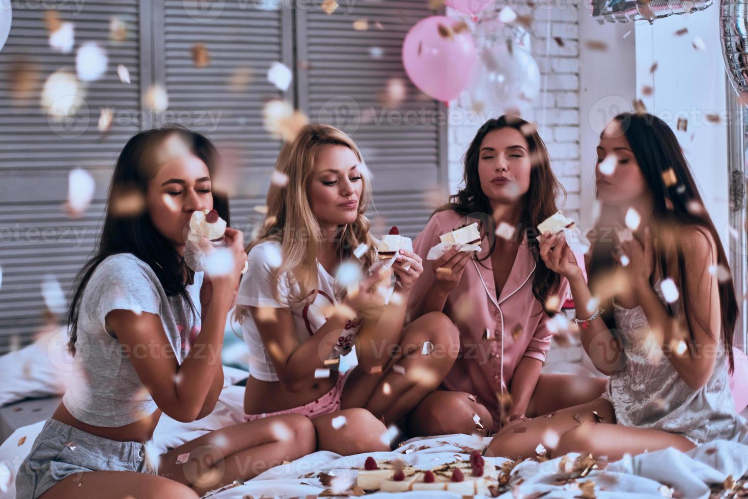 Incredible taste. Four beautiful young women in pajamas eating cake while having a slumber party in the bedroom photo