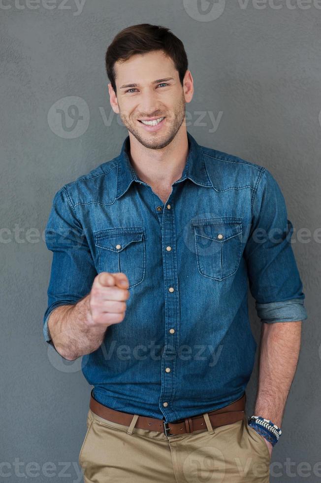 You can do it Happy young man pointing at camera and smiling while standing against grey background photo