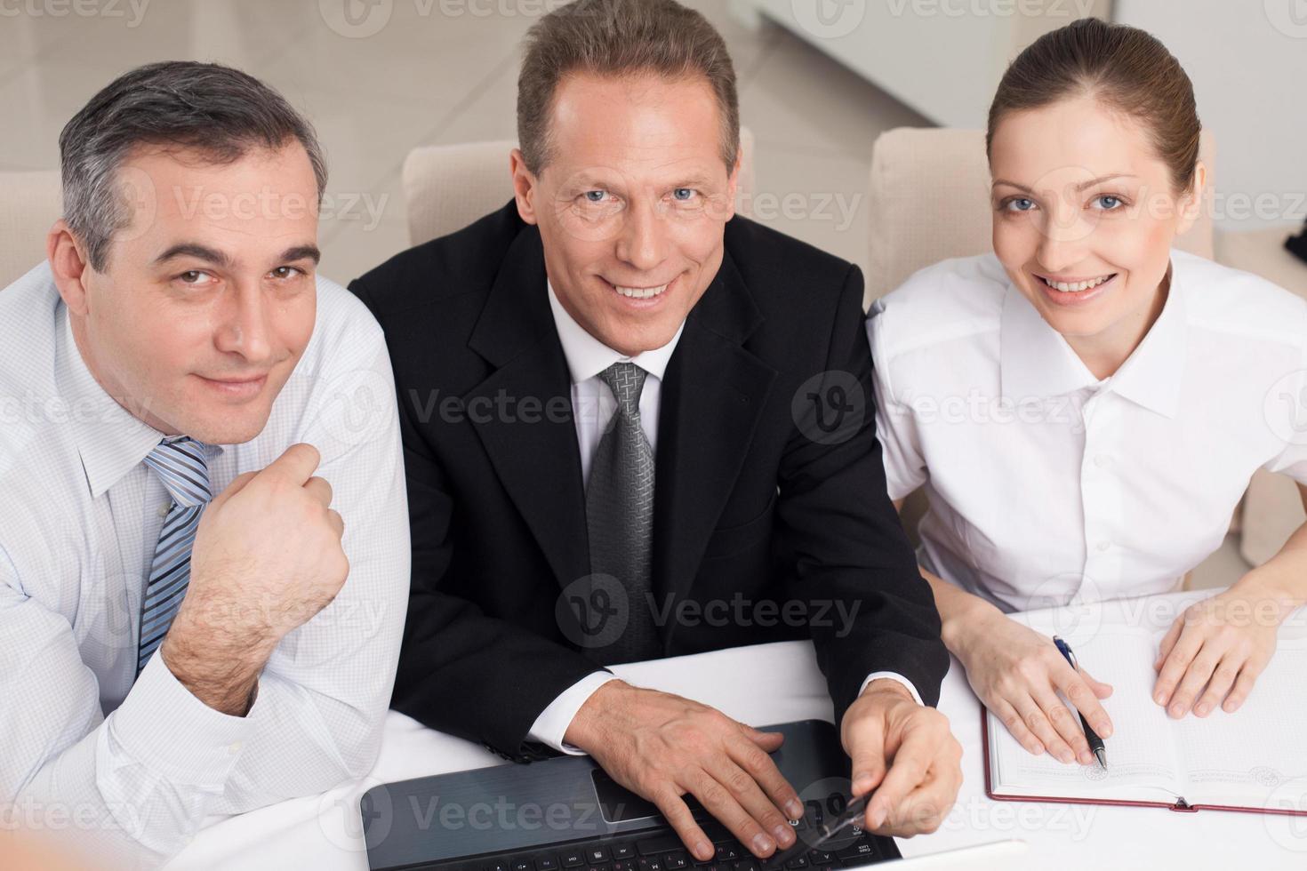 Business people at work. Top view of three cheerful business people in formalwear sitting at the table and looking at camera photo