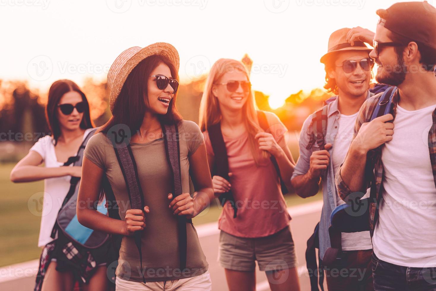 In search of adventures. Group of young people with backpacks walking together by the road and looking happy photo