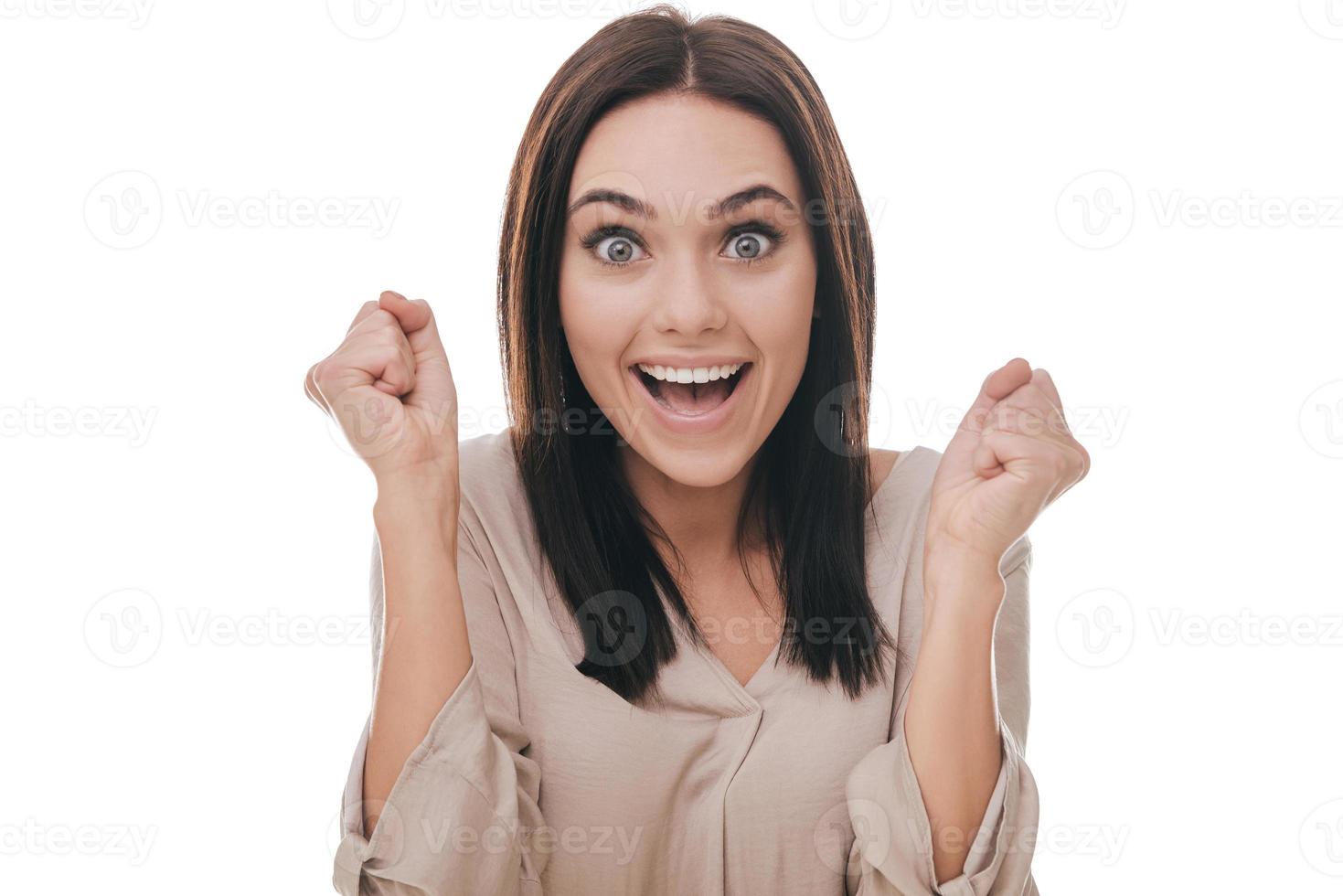 Feeling so happy now. Beautiful young woman gesturing and looking happy while standing against white background photo