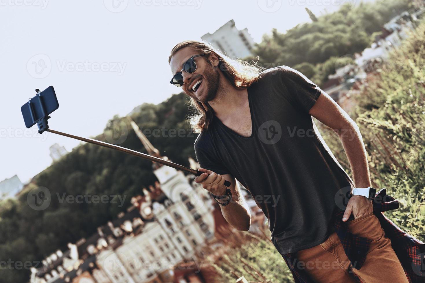 Selfie time. Handsome young man in casual clothing smiling while taking selfie outdoors photo