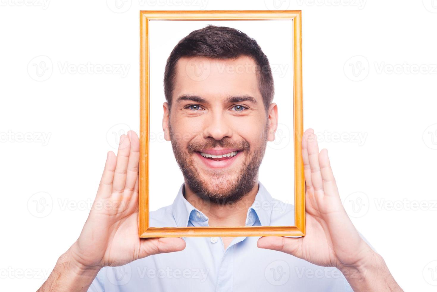 retrato de mí apuesto joven en camisa mirando a la cámara a través del marco de la imagen mientras está de pie contra el fondo blanco foto