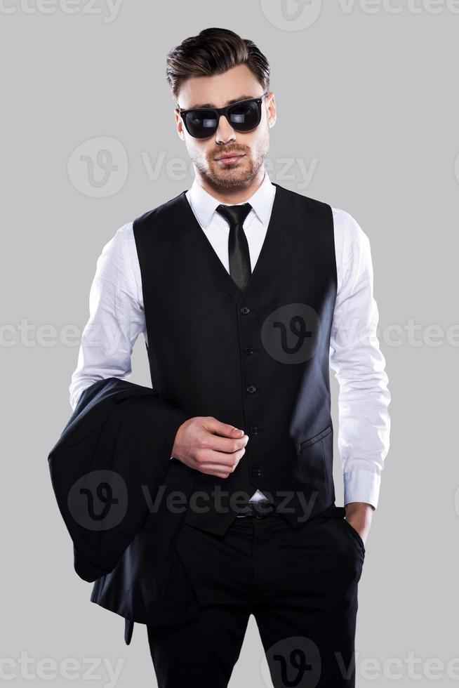 Confident and handsome. Handsome young man in formalwear carrying jacket and looking at camera while standing against grey background photo