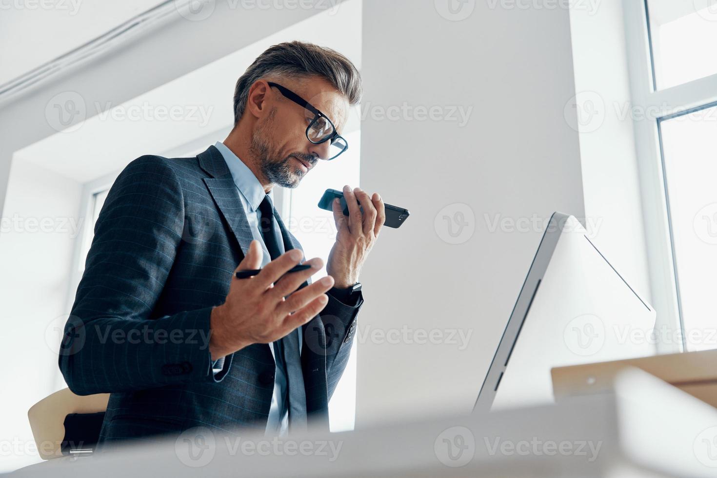 hombre de negocios concentrado que usa un altavoz mientras habla por teléfono móvil en la oficina foto