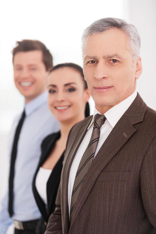 We are successful team. Side view of confident people in formalwear looking at camera and smiling while standing in a row photo