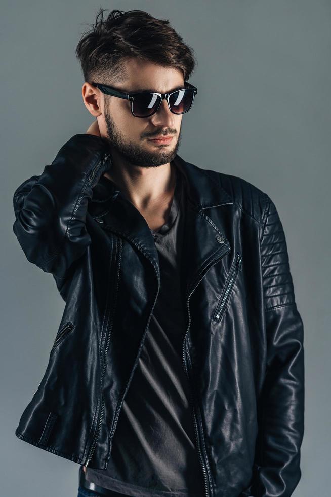 Style and fashion. Confident young man in sunglasses looking away while standing against grey background photo