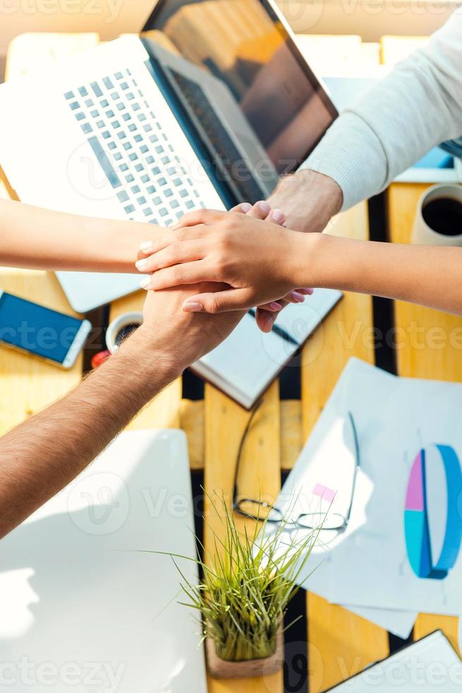 Team spirit. Top view of business people holding hands clasped upon the wooden desk photo